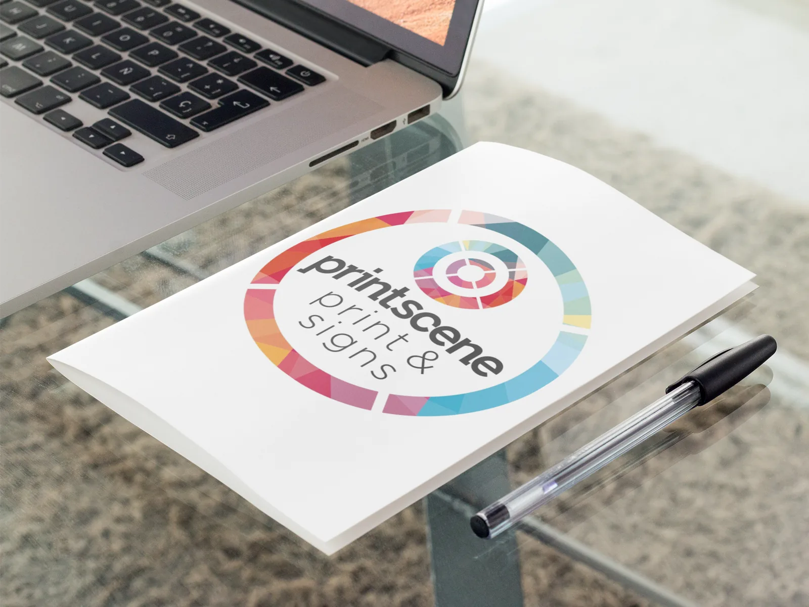 Printscene-branded folded brochure on a glass desk beside a laptop and pen