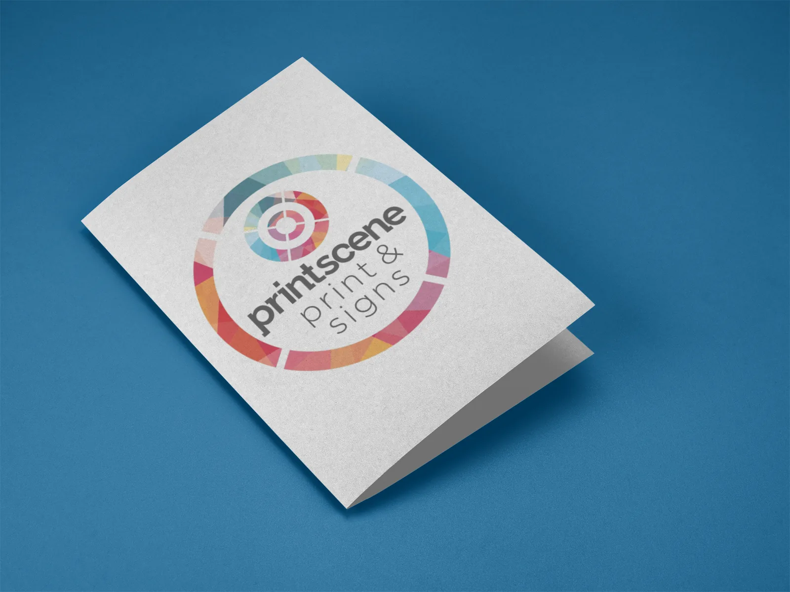 Folded Printscene brochure standing open on a blue surface