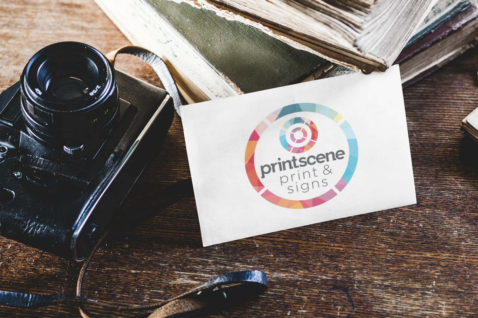 Printscene-branded postcard on a wooden desk beside a camera